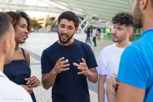 Young man speaks, gesturing with his hands, while others listen.