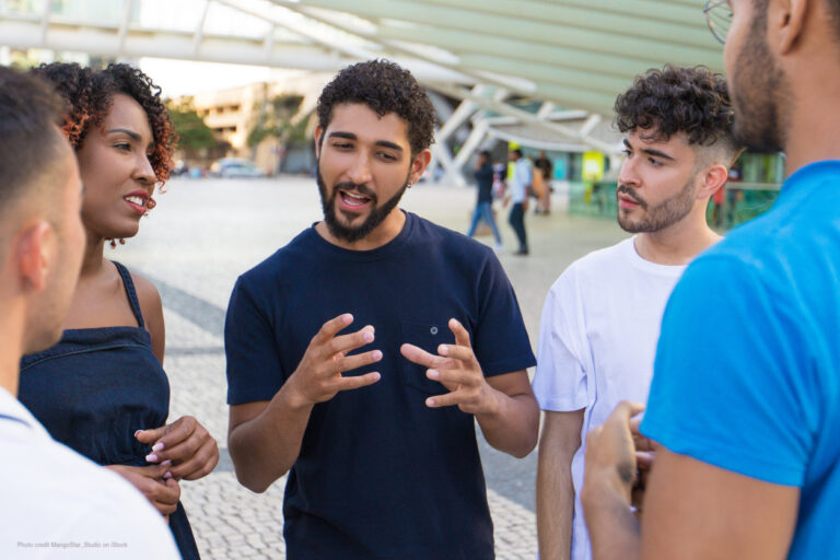 Young man speaks, gesturing with his hands, while others listen.