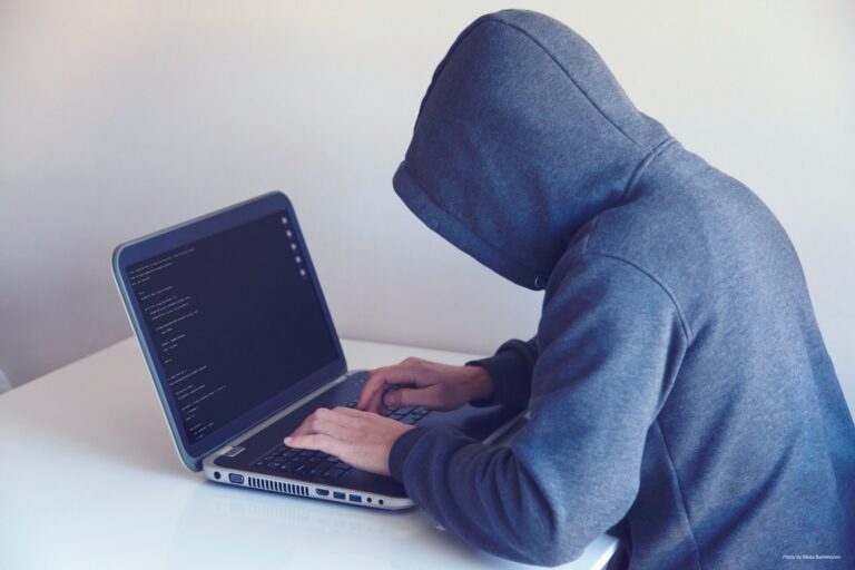 Person with face concealed by hooded sweatshirt types on a laptop.