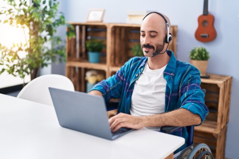 Man with headphones sitting in wheelchair using a laptop.